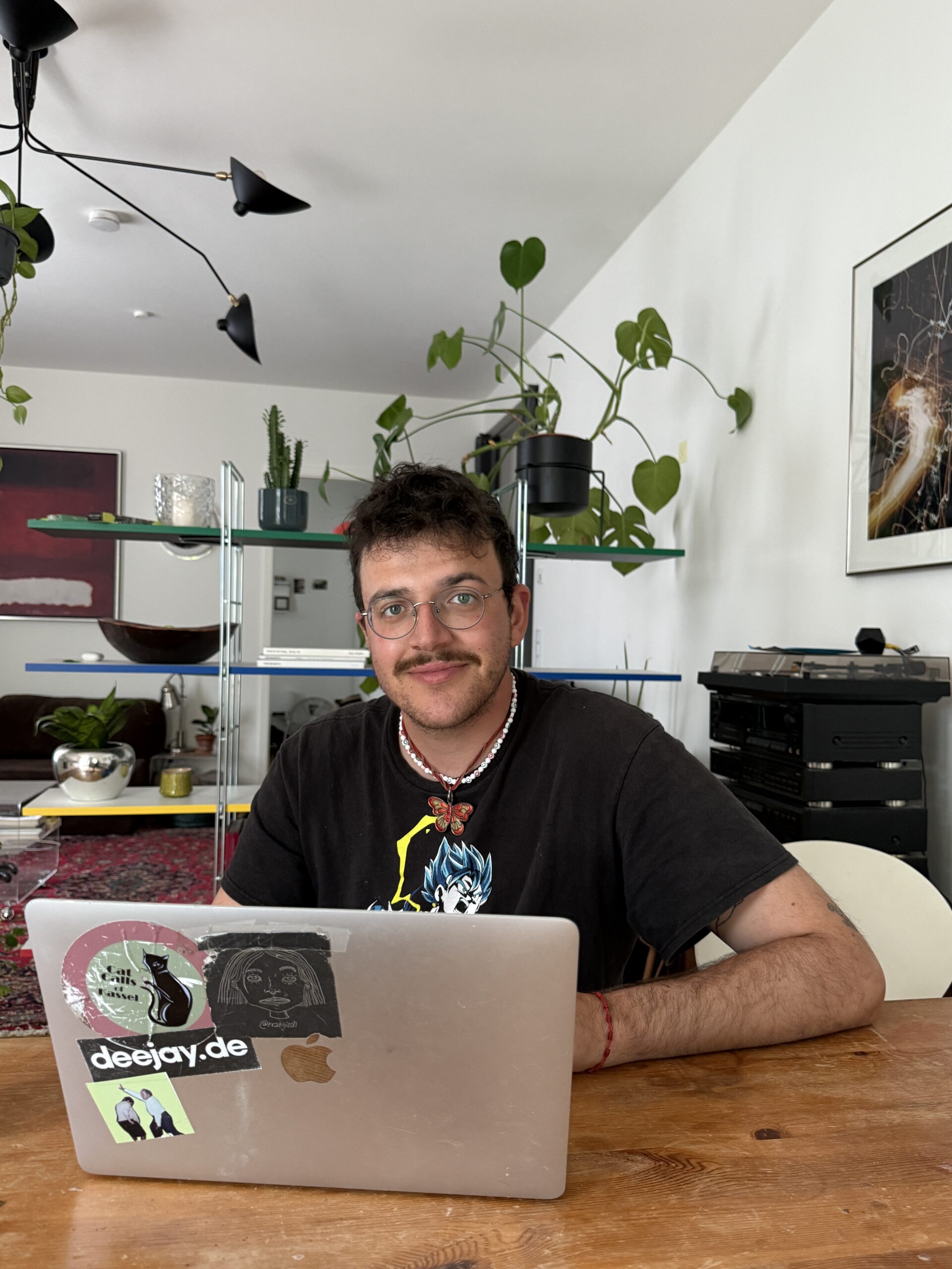 Person sitting at a wooden table working on a laptop in a plant-filled living room.